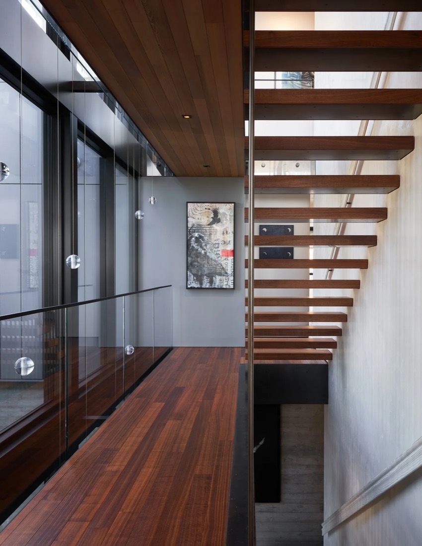 Open-riser stair in oak beside a glass corridor